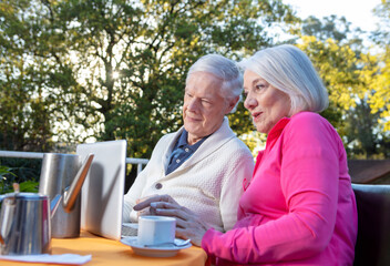 Elderly people living their life at its best. Couple of retired people making breakfast outdoor and using laptop.