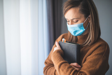 Portrait of a woman with a surgical mask on her face and a bible held tight to her chest - 486945079