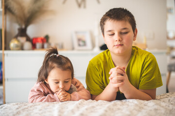 brother and sister praying together in the morning at the edge of the bed