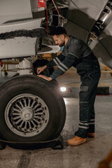 Obraz na płótnie Canvas Full length of bearded man aviation maintenance technician repairing aircraft landing gear at repair station