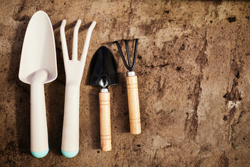 Two pairs of garden shovel and fork made up of white plastic, wood and black metal on shabby brown background