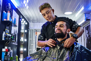 barbero preparando a su cliente para cortarle el pelo y rasurar su barba 