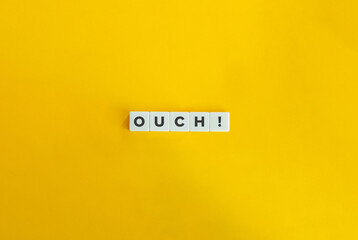 Ouch Word on Letter tiles on yellow background. Minimal aesthetics.