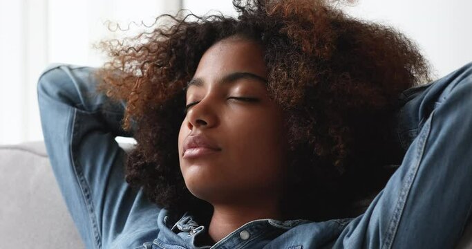 Fatigue relieve, stress-free day, comfort smart house, daydreams concept. Close up face beautiful carefree curly-haired African teenage girl closed eyes put hands behind head relaxing alone at home