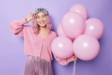 Horizontal shot of positive woman smiles broadly has long dyed pink hair dressed in festive clothes...