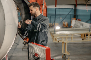Bearded man aviation maintenance technician using screwdriver while repairing airplane in repair station