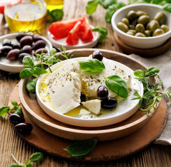 Feta cheese with the addition of olive oil, olives and herbs on a ceramic plate on a rustic table. Traditional Greek products