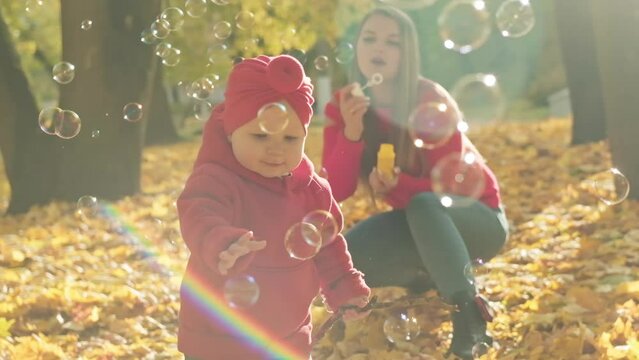 Happy mother and daughter having fun with bubbles in autumn park. Carefree childhood. Laughing child with mother outdoors in slow motion