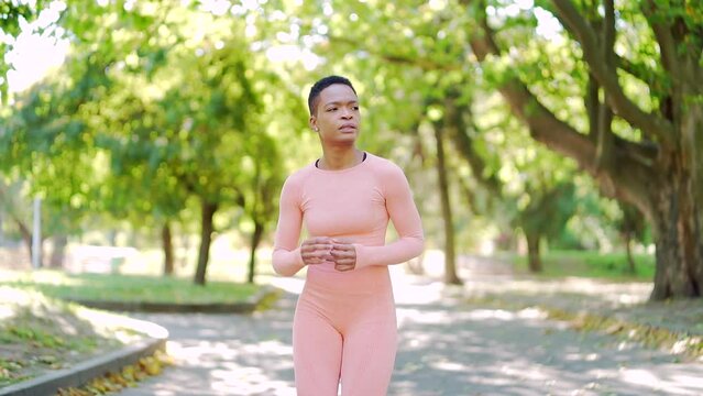 young african american slim woman runner jogging in the morning on urban park in pink tracksuit. Active healthy lifestyle. Black female athlete runs outdoors in the city. Nature between green trees