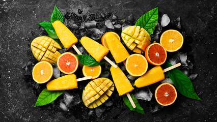 Tropical fruit popsicles on ice. Cold summer fruit sweets. On a black stone background. Top view.