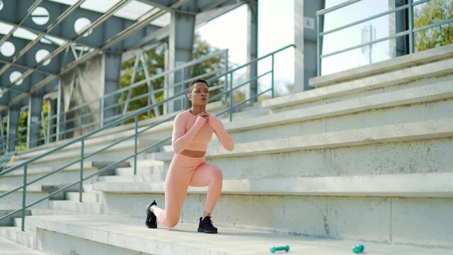 African american fitness sport woman athlete engaged in workout. outdoors. in modern urban stadium. Black female jumps and squats on the city streets. outside. Morning cardio warm-up. Active lifestyle