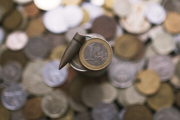 Stack of coins with euro coin and bullet on top with coins blurred background