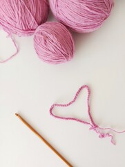 Pink balls of yarn on a white background. A set of a chain of air loops with a bamboo crochet. Pink yarn heart. Crochet. vertical orientation