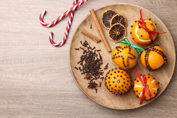 Pomander balls made of tangerines with cloves and candy canes on wooden table, flat lay. Space for text