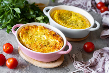 Breakfast for the family: Omelet with cheese and spices, baked in the oven in beautiful ceramic molds on a gray table. Close-up