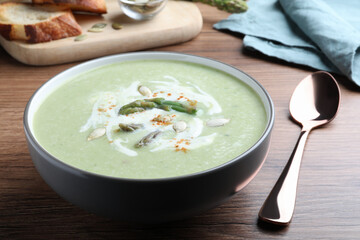 Delicious asparagus soup with pumpkin seeds served on wooden table, closeup