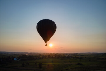 Aerial view of big hot air baloon flying over rural countryside at sunset