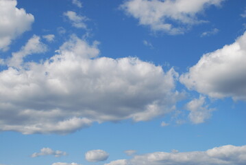 White clouds in a clear blue sky. Small cumulus clouds float across the light blue sky. They form a small group next to each other. Clouds of various shapes and sizes.