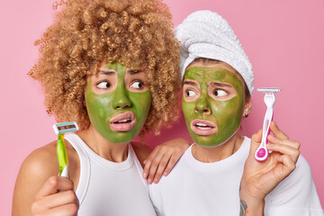 Embarrassed two young women hold razors going to do hygiene procedures shave legs apply green...