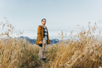 The guy is a photographer in the field, against the background of mountains, takes a picture on an old retro film camera. Man walks in the fall in casual clothes. Concept lifestyle millennial hipster