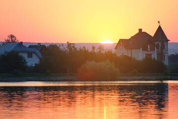 Dark silhouette of suburban houses in front of lake water at bright sunset
