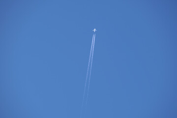 Distant passenger jet plane flying on high altitude on clear blue sky leaving white smoke trace of contrail behind. Air transportation concept