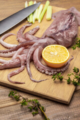 Raw squid with tentacles, lemon and knife on cutting board.