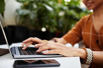 Hands of young biracial woman typing on laptop keyboard while searching for new equipment for...