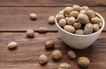 Bowl with nutmeg seeds on wooden table, closeup. Space for text