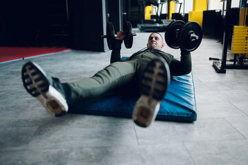 Fototapeta na wymiar Man lying on the mat in the gym and training with dumbbell