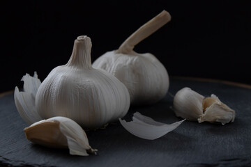 Two bulbs of garlic lie on a kitchen cutting board. Close-up. Daytime lighting.