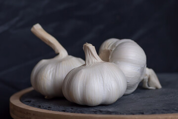 Three bulbs of garlic lie on a stone cutting board. Close-up. Black background with place for text. Copy paste.