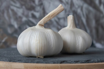 Two bulbs of garlic lie on a stone cutting board. Close-up.