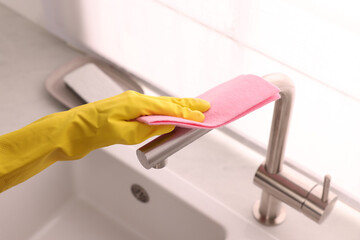 Woman in gloves cleaning faucet of kitchen sink with rag, closeup