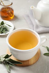 Cup of aromatic sage tea and fresh leaves on light grey table