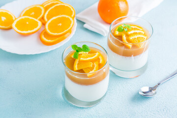 Orange panna cotta with mint leaf in glasses and orange slices on a plate on a light table. Sweet Italian dessert
