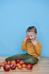 Fototapeta premium a boy of 2 years sits on a wooden table and plays with apples and tangerines, he closes his eyes and plays a game.