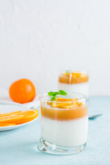 Panna cotta with orange and mint leaf in glasses on a light table. Sweet Italian dessert. Vertical view