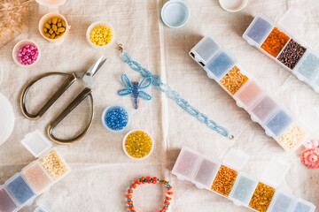 Items for beading - boxes with beads, thread and scissors on the table. Development of creative skills and fine motor skills for children. Top view.