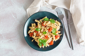Ready to eat pasta with tomatoes and basil on a plate and ingredients on the table. Mediterranean cuisine. Top view