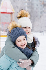 Fototapeta premium Two smiling girls in warm clothes are hugging in a snowy city. Winter walks, lifestyle. Vertical view