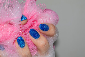 Fototapeta premium A woman's hand holds a soapy pink sponge. Reflective blue manicure.