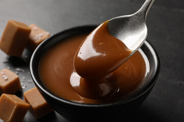 Taking yummy salted caramel with spoon from bowl on table, closeup