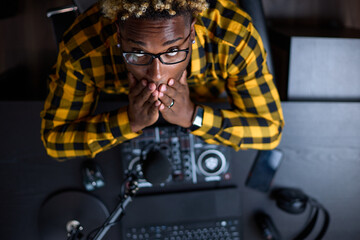 Top view of a young African man sitting with his hands on his face in a recording studio. Black radio host or musician has a problem, the guy made a mistake on air or inspiration does not come to him.