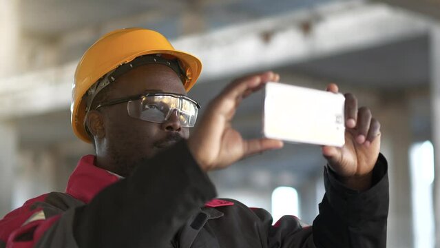 Slow Motion Afro-american worker records videos on his smartphone. Builder at construction site filming a video