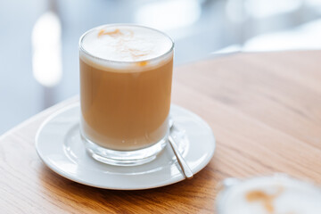 Caffe latte in transparent mug with other mug in first plan, blurred. Barista coffee for international barista day. Break and pause to chill. Coffee with milk and foam. 