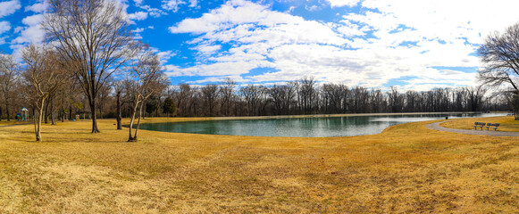 a panoramic shot of a still green lake surrounded by yellow winter grass and bare winter trees with...