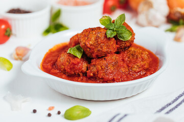 Meatballs in tomato sauce with basil on top. Bright background with ingredients in blurry background. This meal is called Kofte in Turkey and Cufte in Balkans. International meatball day.