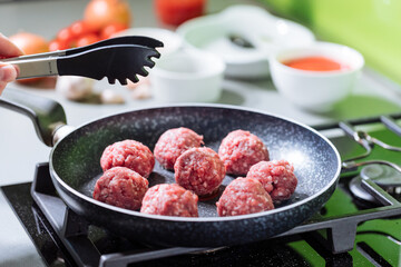 Meatballs in tomato sauce with basil on top. Bright background with ingredients in blurry background. This meal is called Kofte in Turkey and Cufte in Balkans. International meatball day.