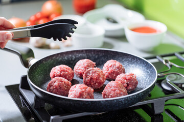 Meatballs in tomato sauce with basil on top. Bright background with ingredients in blurry background. This meal is called Kofte in Turkey and Cufte in Balkans. International meatball day.